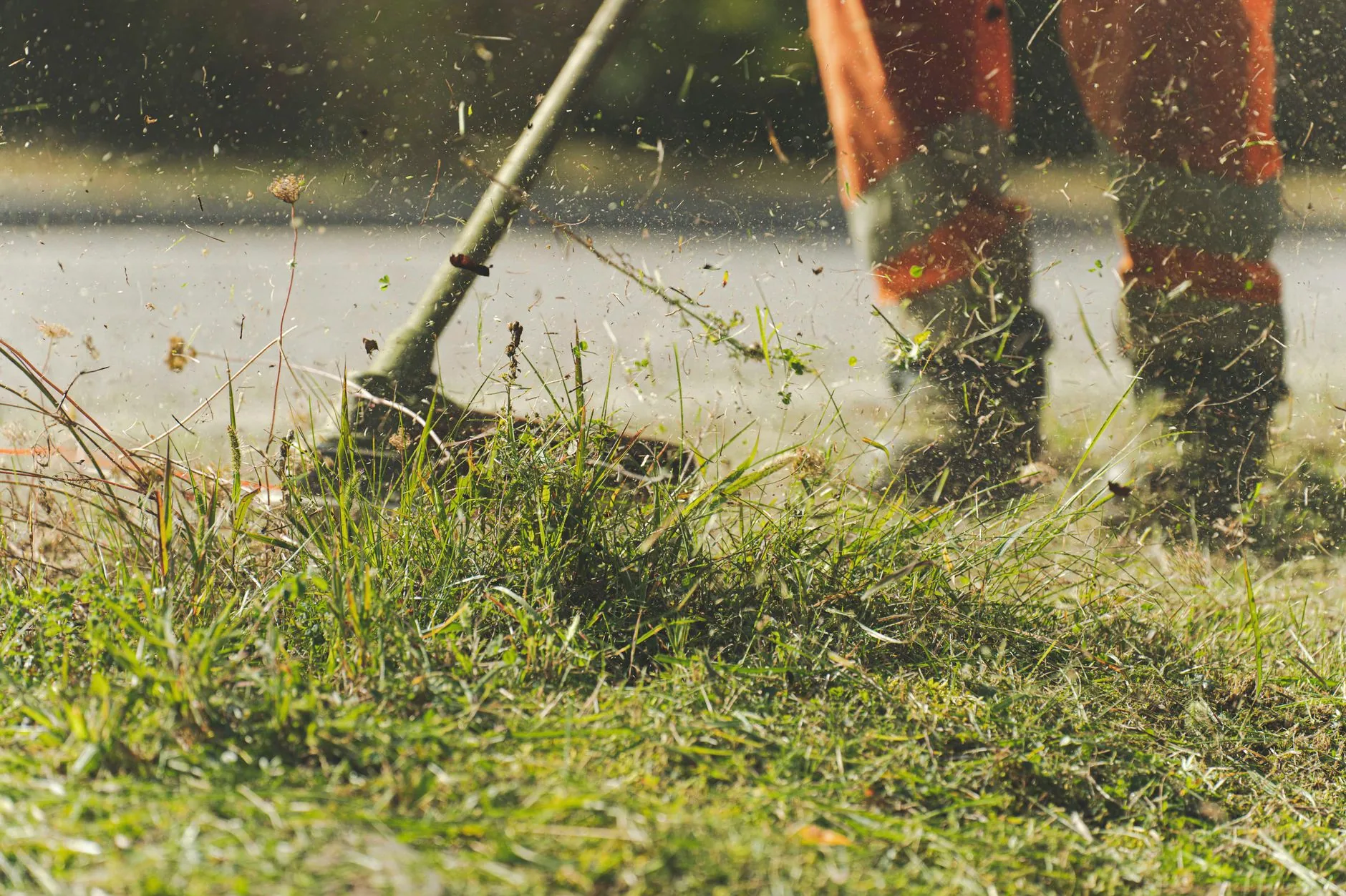 Line trimmer cutting long grass along a kerb edge