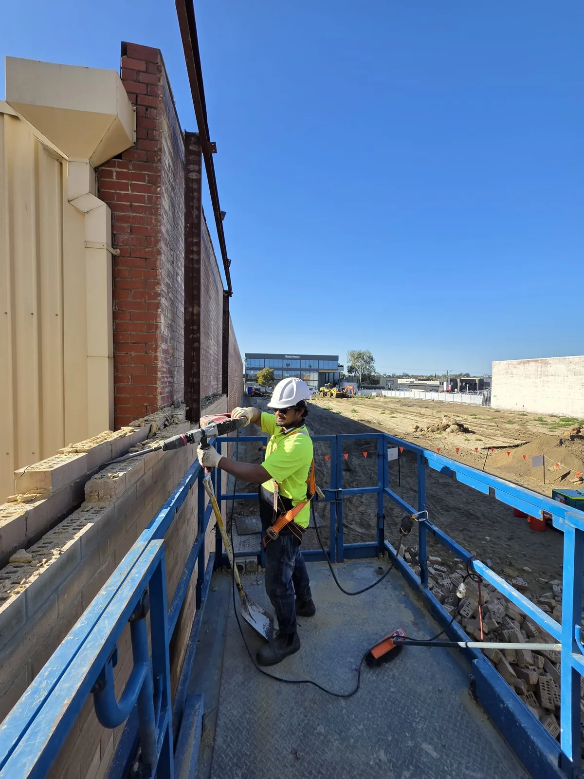 Worker in hi-vis and hard hat removing a brick wall from an elevated work platform on a Perth commercial site