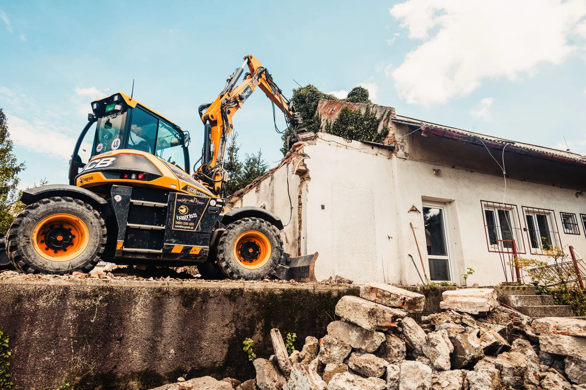 Excavator demolishing a small building and clearing the rubble